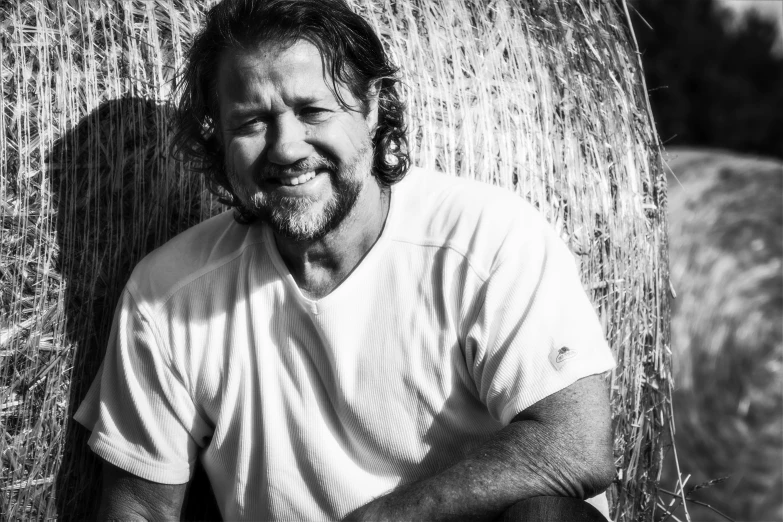 man smiling while leaning against hay bale