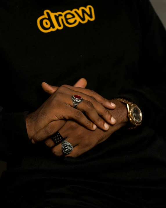 close up po of a man wearing multiple rings and black shirt