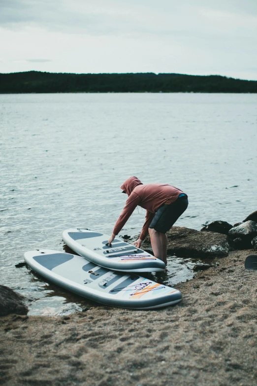 a man bent over on surfboards next to the shore