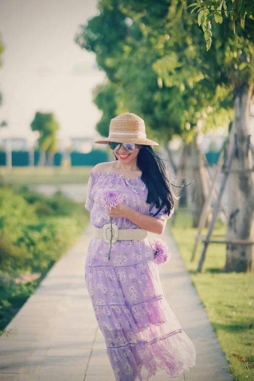 woman in large hat and sunglasses holding flower in field