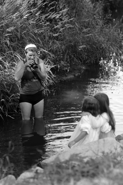 three people wading in the river near some grass