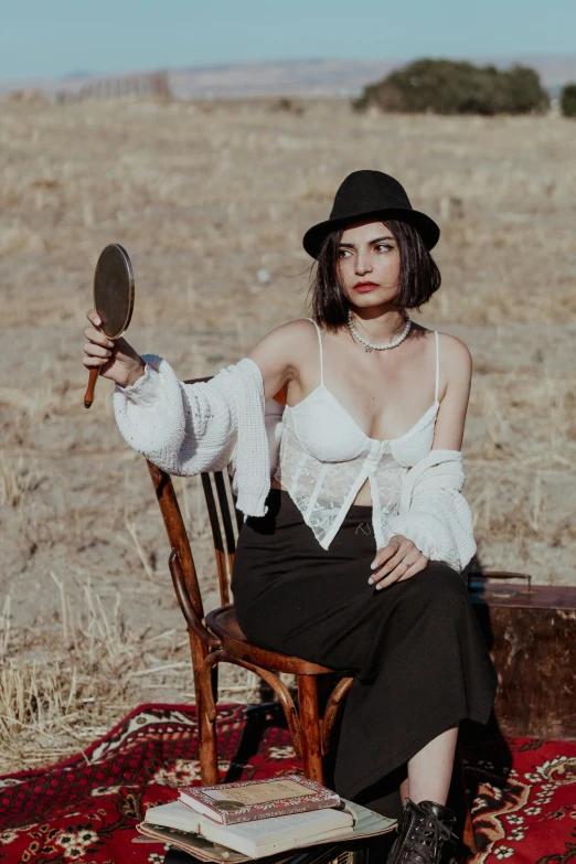 a young woman poses for a picture in a chair with a hat and long sleeves