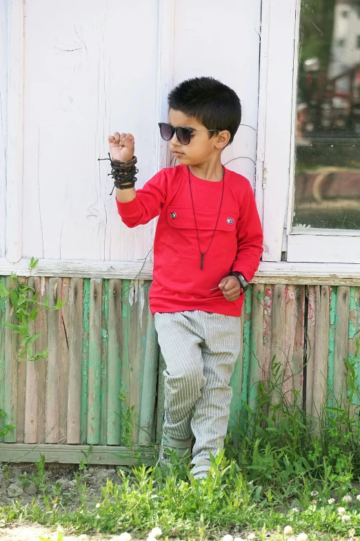 a little boy in sunglasses standing by a white wall