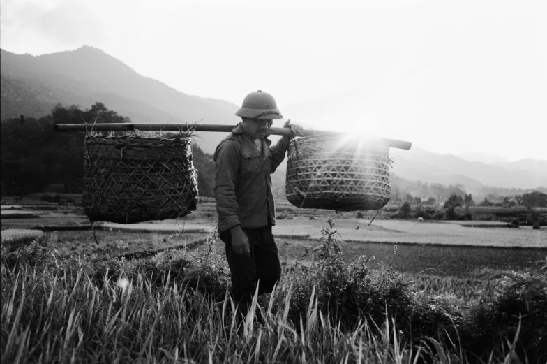 a man with a hat and sunglasses carrying large baskets on a farm