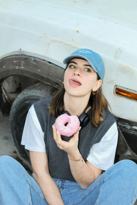 woman holding a donut while wearing a cap and jeans