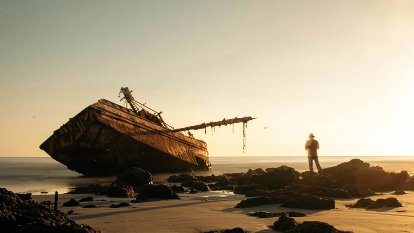 a man looking up at the top of a boat washed on a rocky beach