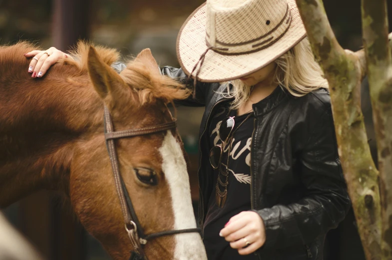 woman with hat touching head of horse on a sunny day