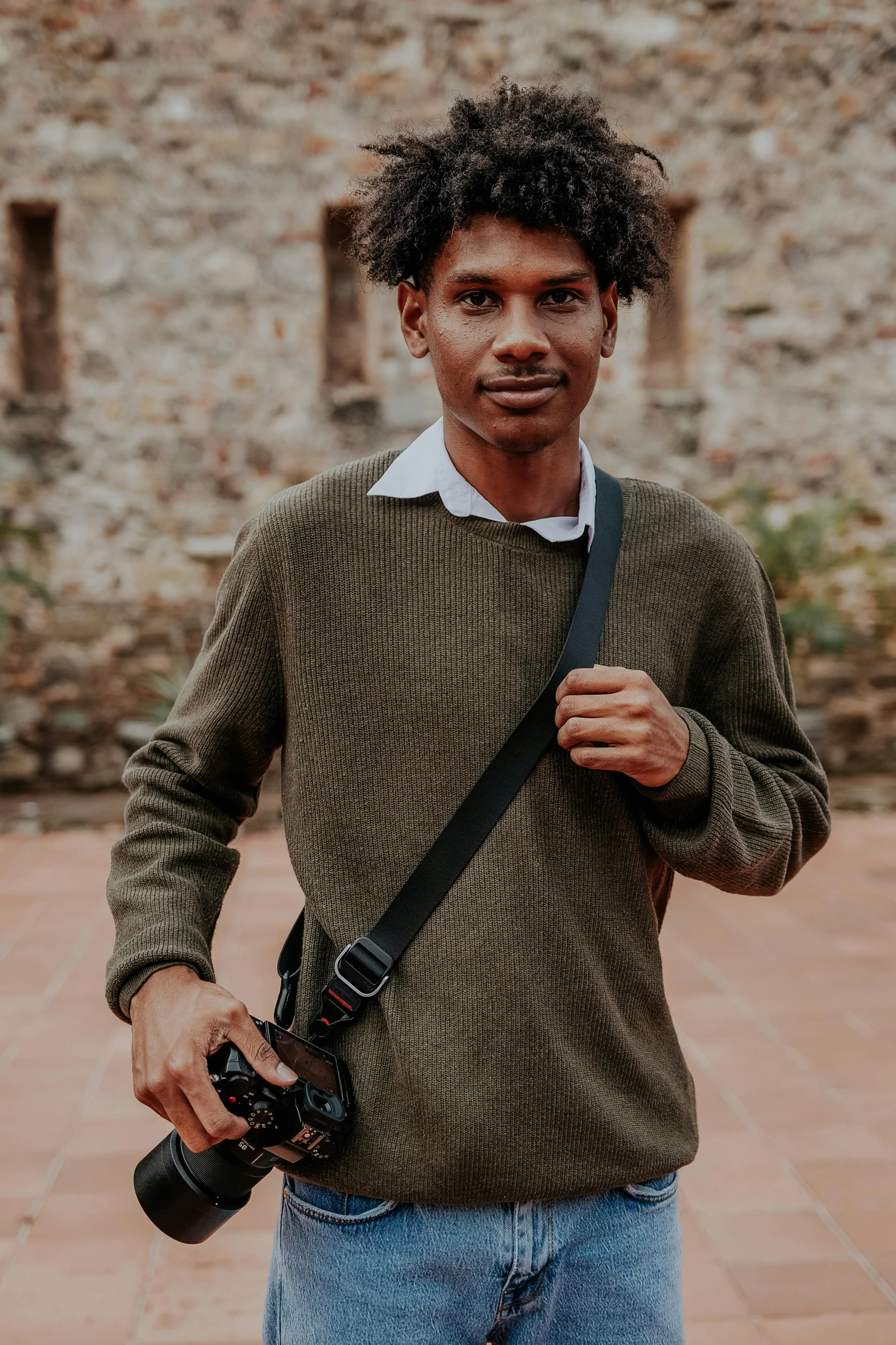 a man holding a camera bag standing next to a stone building