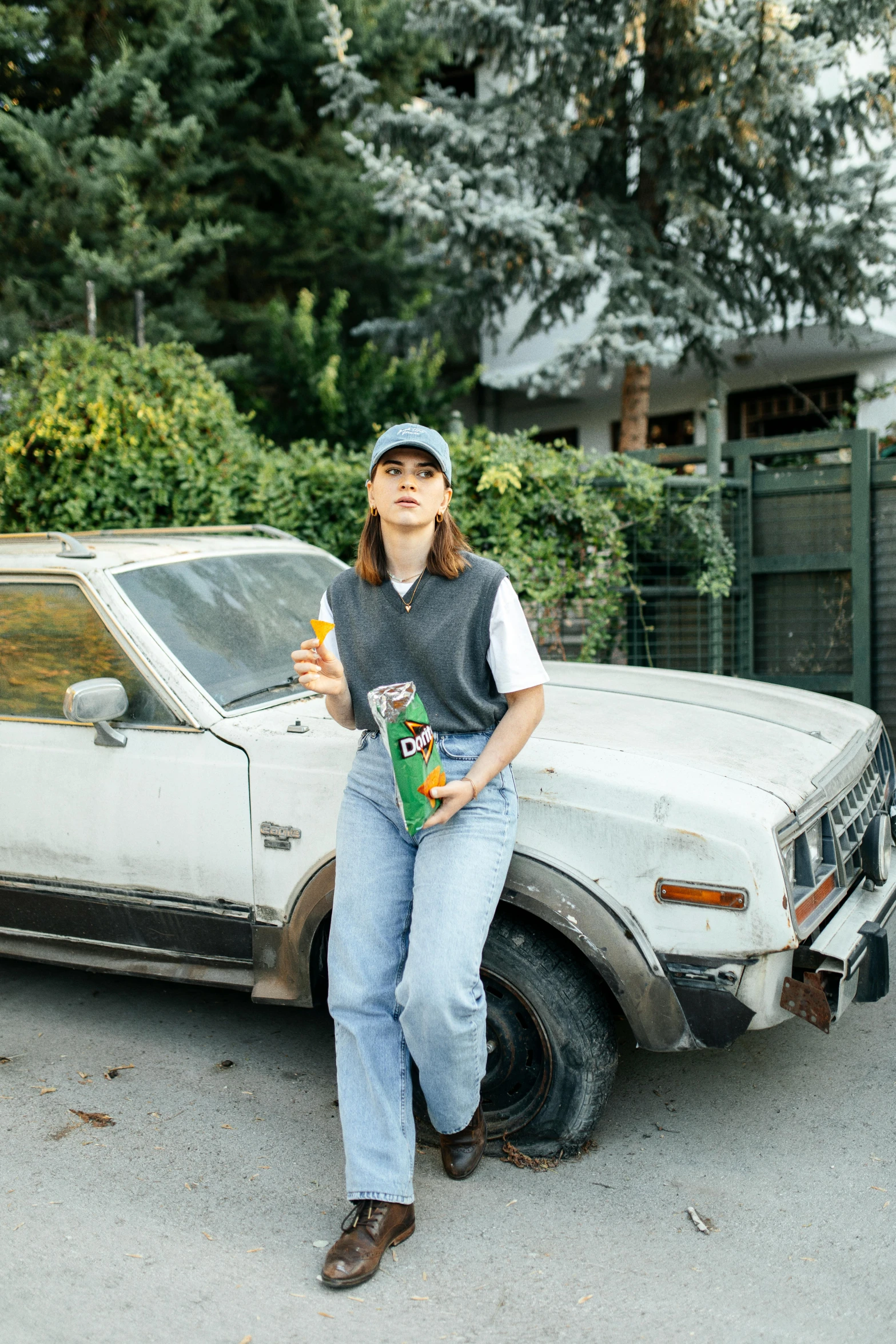 a man sitting on the hood of a white car and holding two drinks in his hands