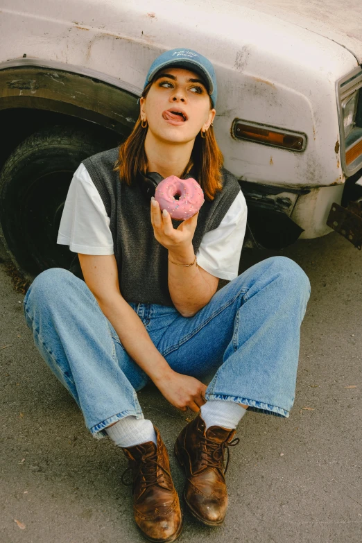 a young woman eating a pink donut while sitting on the ground