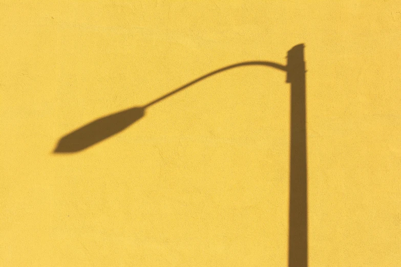 the shadow of a street lamp over yellow pavement