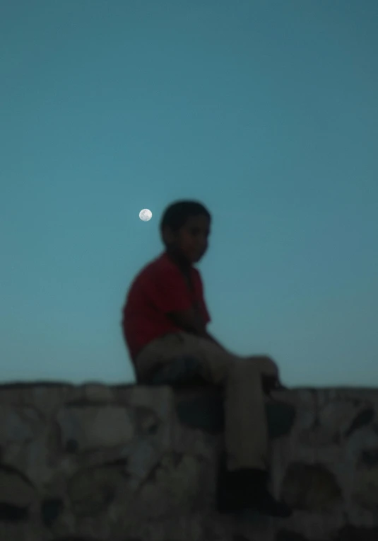 a man sitting on top of a stone wall under a moon