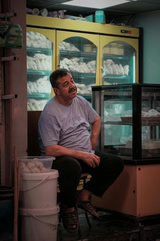 a man sitting on top of a bucket next to a shelf full of food