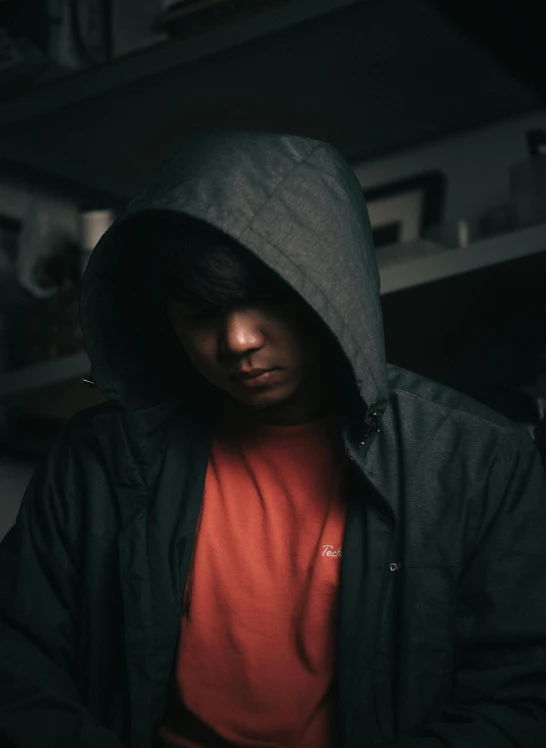 man with hooded jacket looking down at cell phone