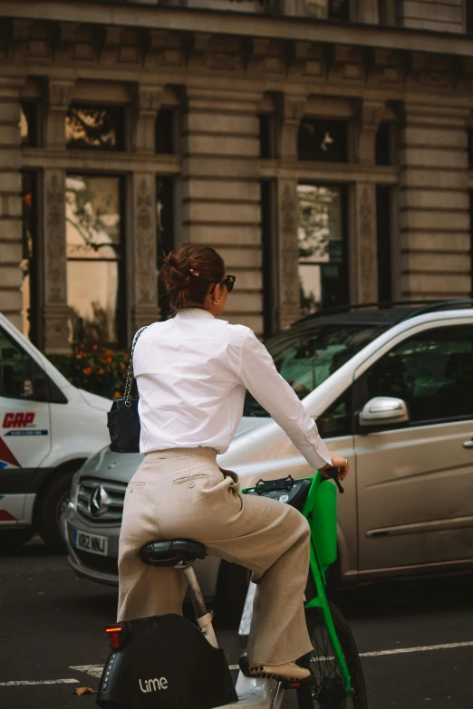 a woman sitting on the back of a bike with a green bag