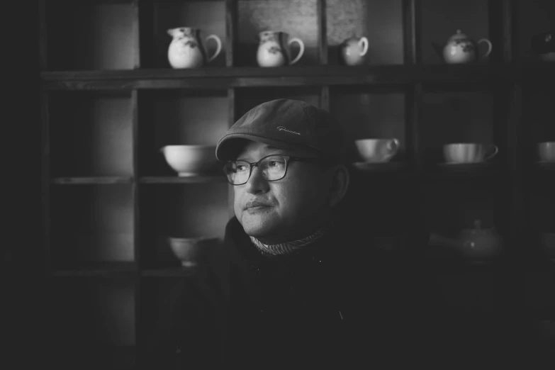 a man in glasses sits in front of many tea pots