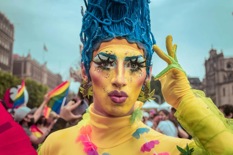 a woman with blue hair and yellow makeup is holding her hand up to the side