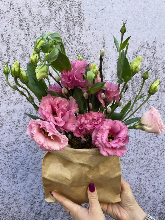 a person holding a flower vase with pink flowers