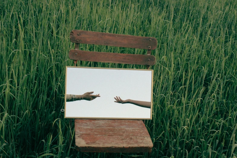 a wooden chair with a mirror showing two hands, and one laying in grass