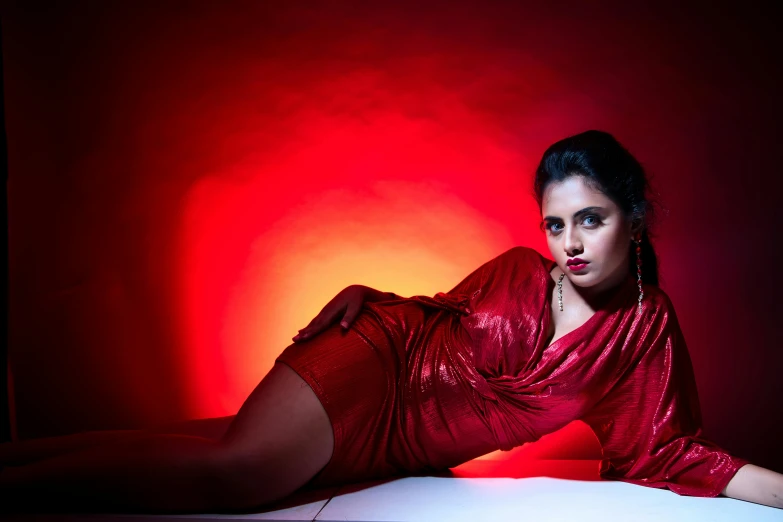 a woman in shiny clothing laying on a bed in front of a red background