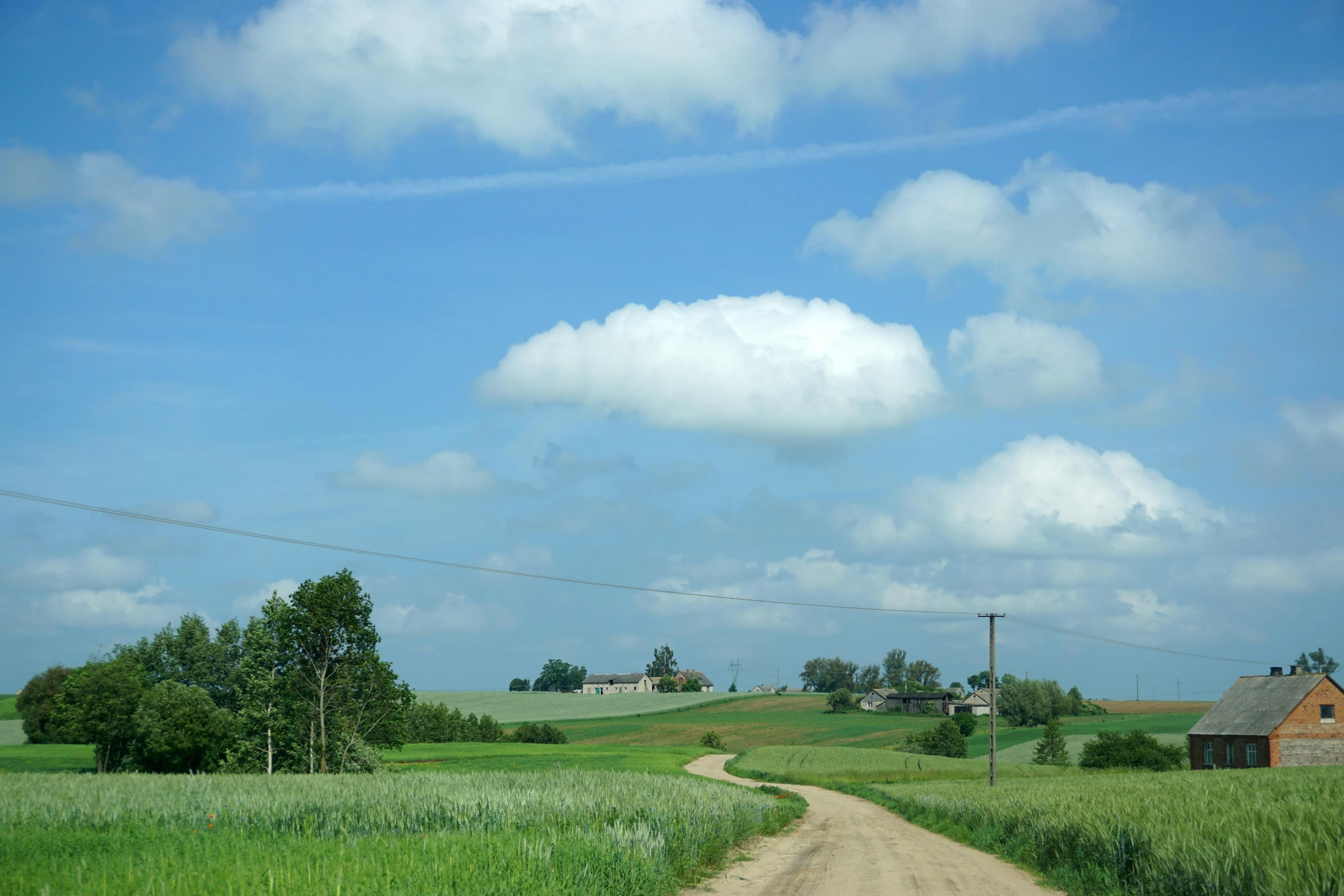 a road and a rural landscape under a cloudy blue sky