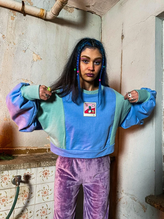 a girl wearing a blue, green, and purple sweatshirt stands in front of a bathroom