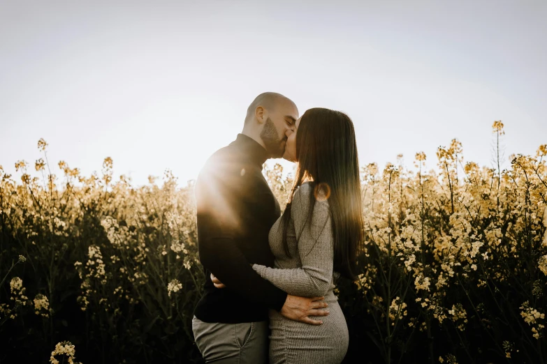 an engaged couple emcing in a field at sunset