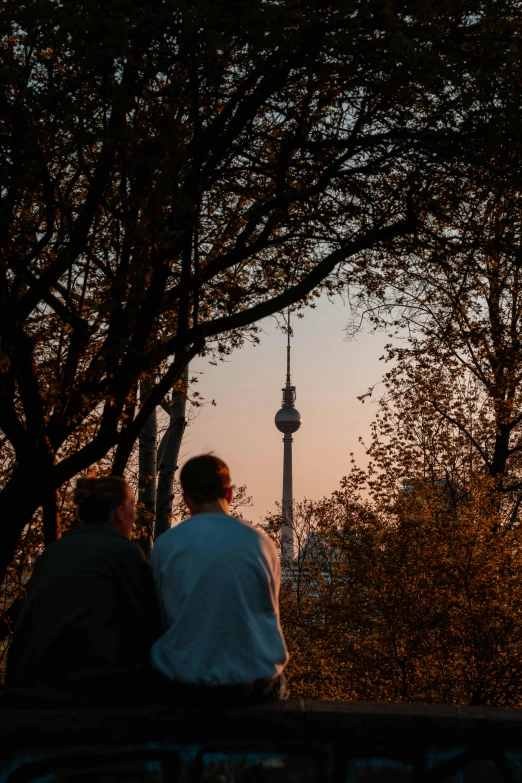 two people sit on a park bench as the sun sets