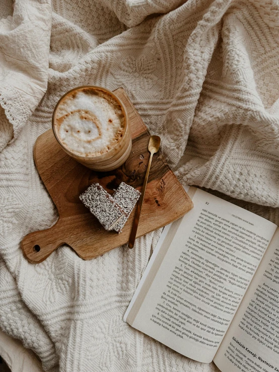 an open book and cappuccino on a table with white blanket