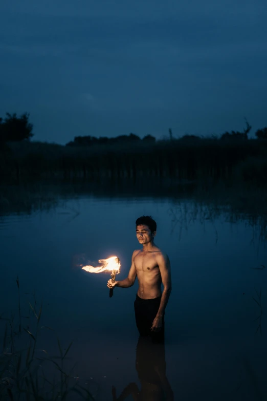 a young man holds a fire show while standing in water at night