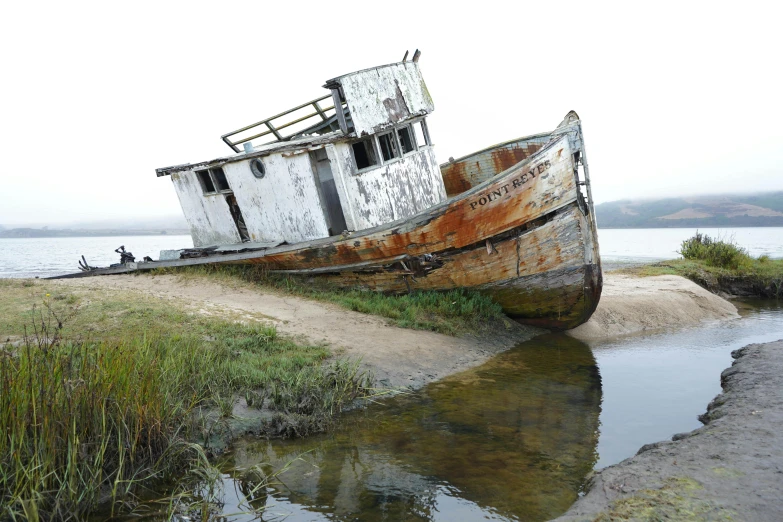 an old boat sits on land near a lake