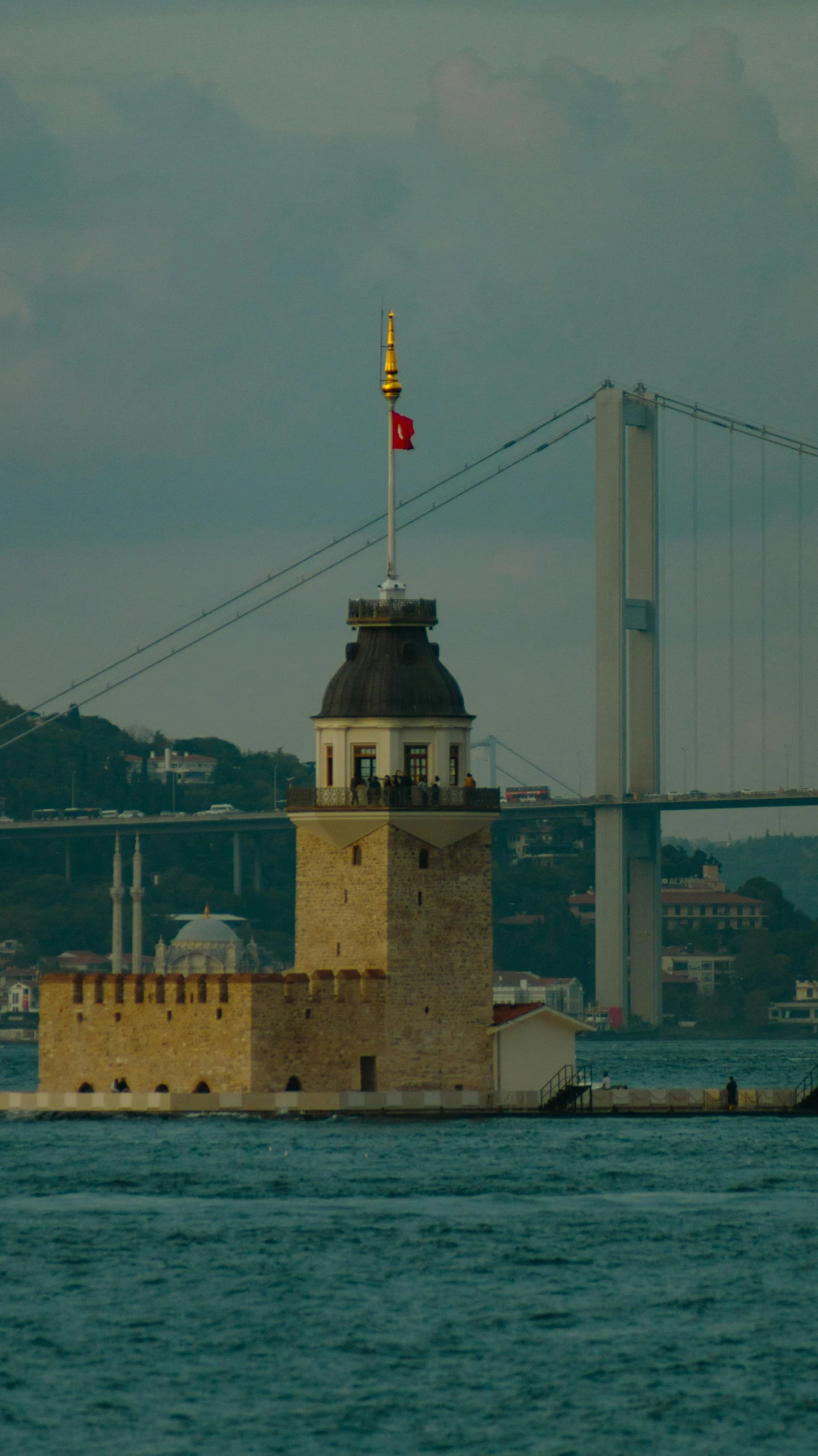 a body of water with a light tower and bridge in the distance