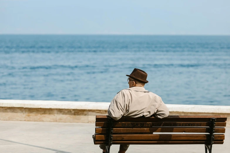 a person is sitting on a bench by the ocean