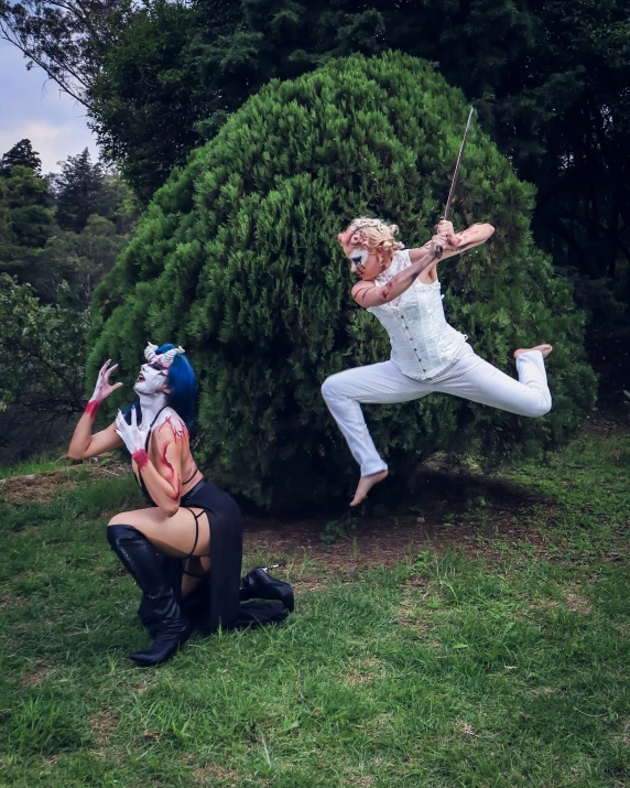 two circus performers performing on green grass in front of trees