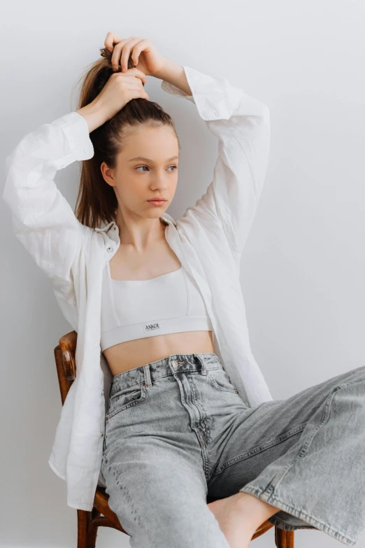 a girl is sitting on a chair and holding her hair up in front of her