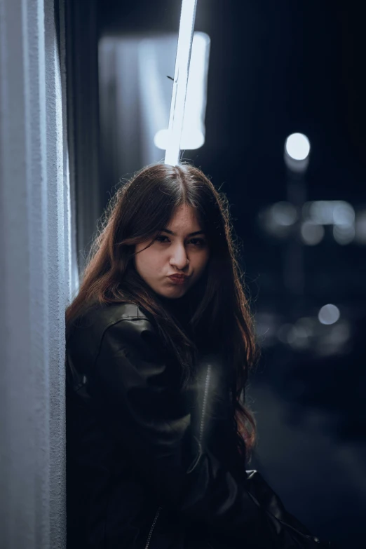 woman in black jacket standing against a wall by streetlight