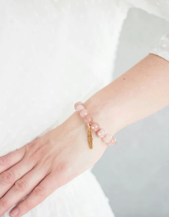 the gold feather charm is on the wrist of a bride