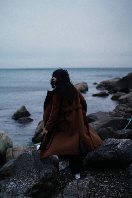 a woman walks along the water on the rocks