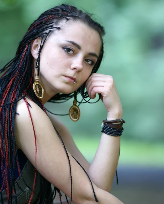 young woman with dreadlocks and gold hoop earrings sitting outdoors