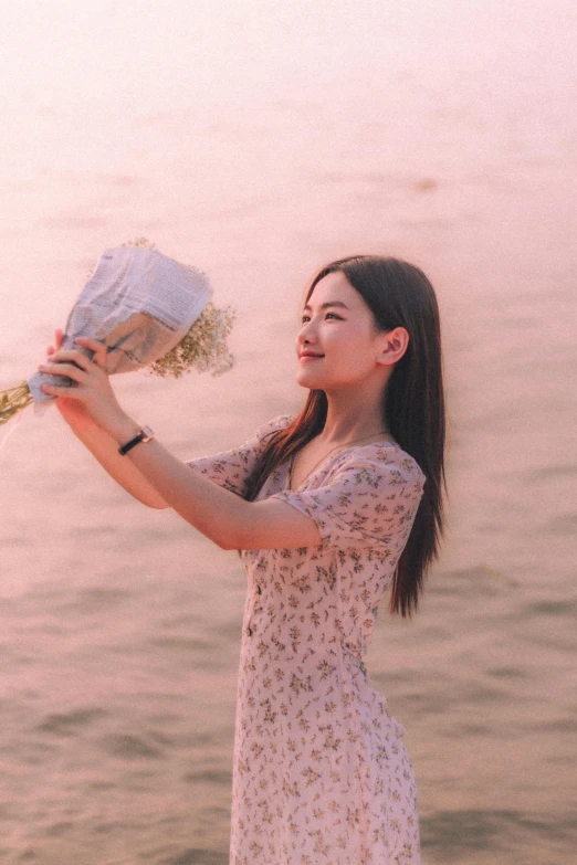 the woman holds flowers over her face at the water's edge