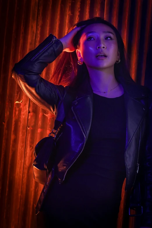 a woman in leather jacket standing next to orange curtains