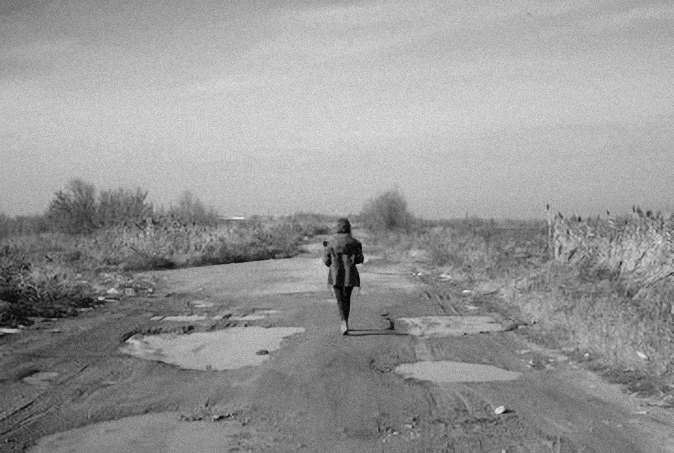 the woman is walking alone along the dirt road