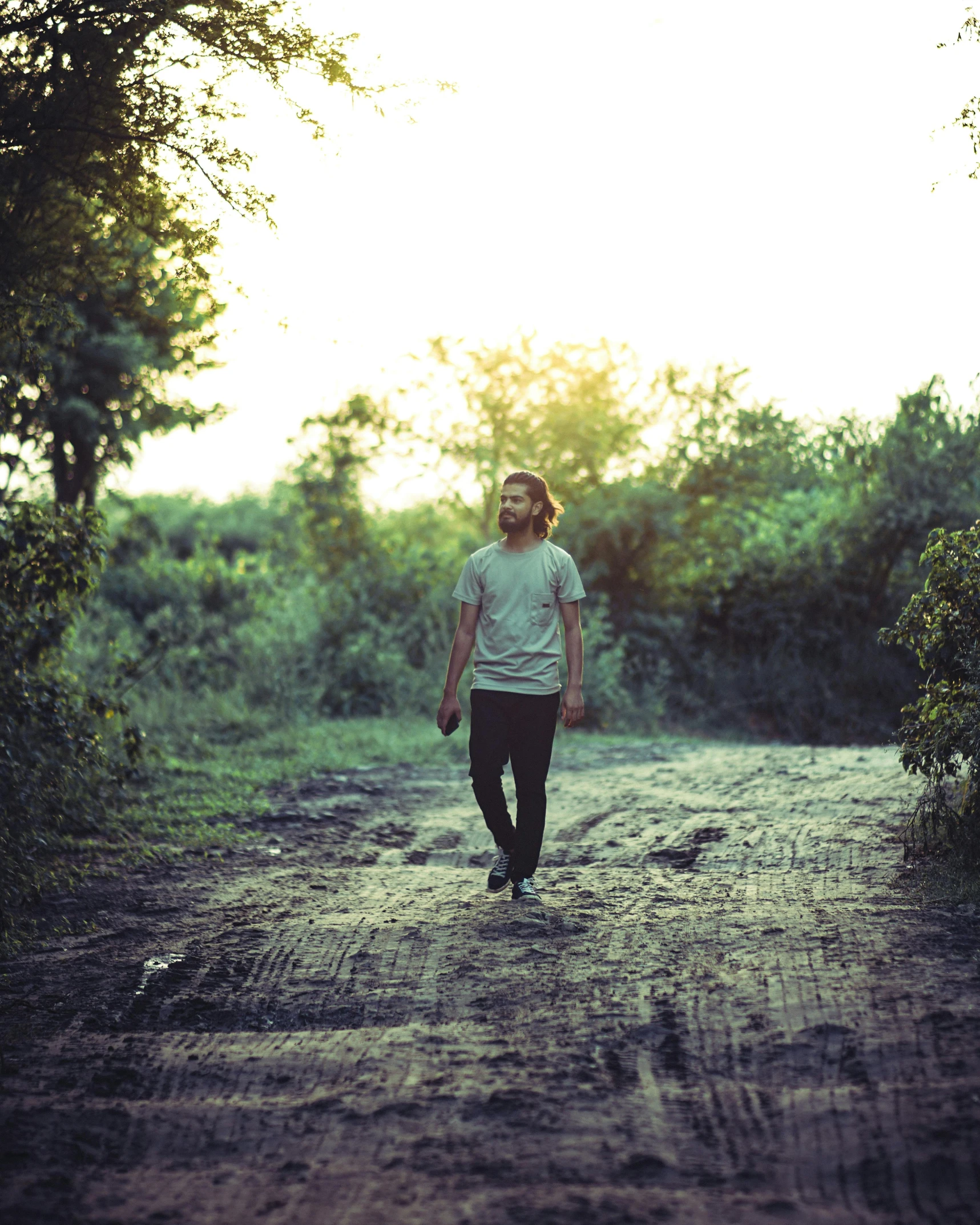 a young man is walking down the dirt road