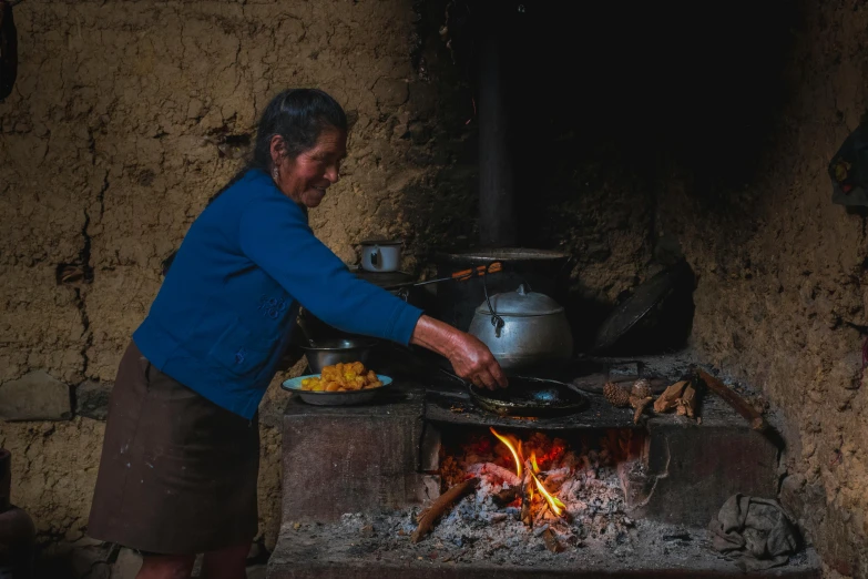 an elderly woman cooks food over an open fire