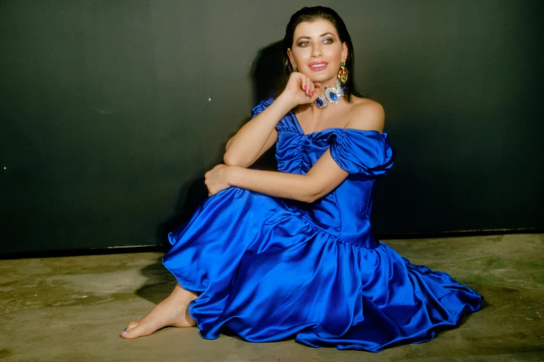 a woman wearing a blue dress poses in front of a dark wall