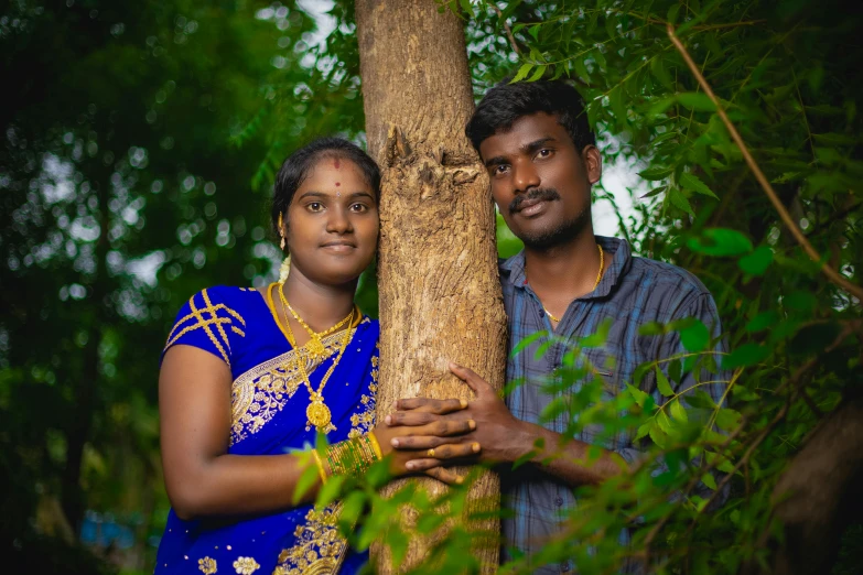 a couple hugging each other by the trunk of a tree