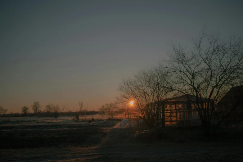 sunset over a snowy field with trees and building