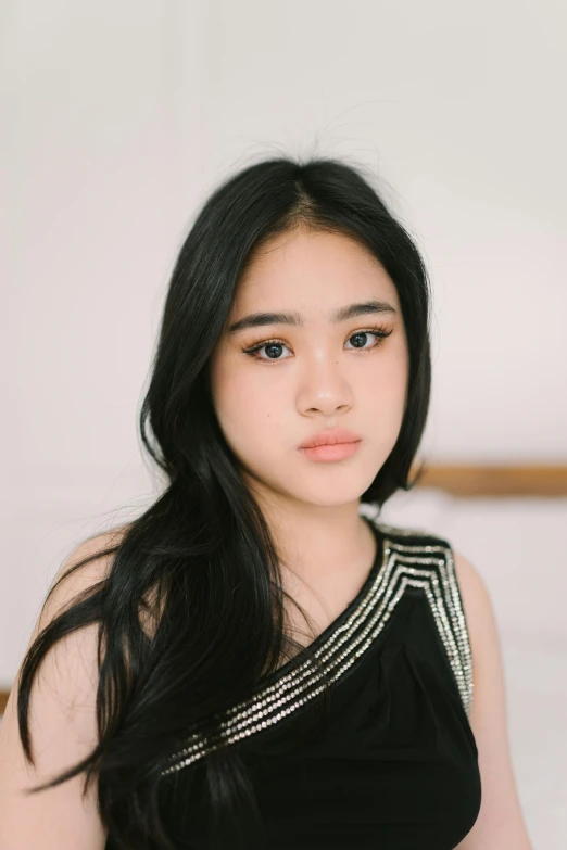 an asian woman in black dress standing near a bed