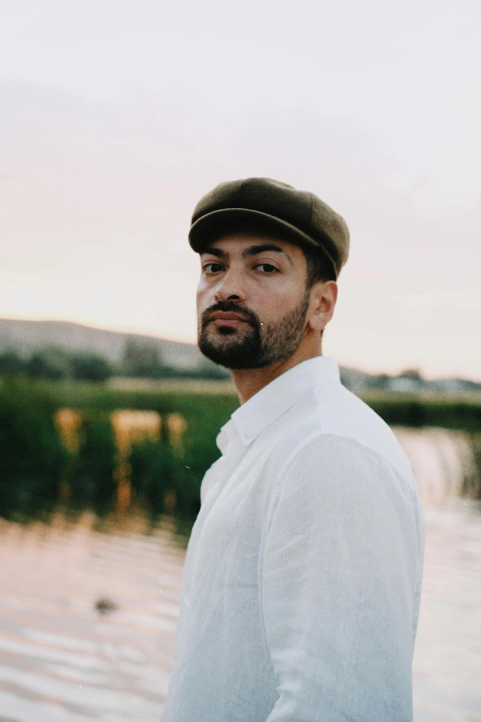 a man wearing a hat and beard is posing by a pond