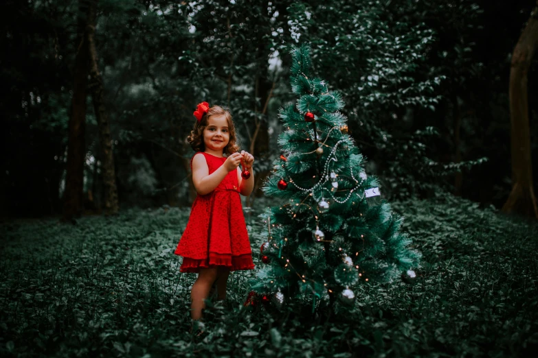 a little girl is posing by a christmas tree